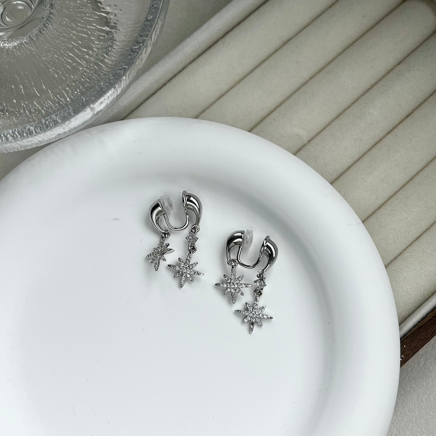 Two silver star front-and-back drop clip-on earrings resting on a branded jewellery display card
