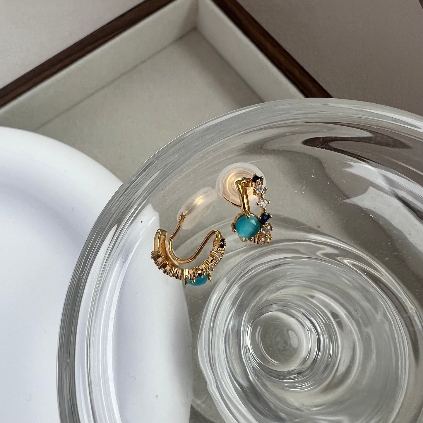A pair of tiny blue gemstone and diamond double hoop clip-on earrings resting on a neutral linen background