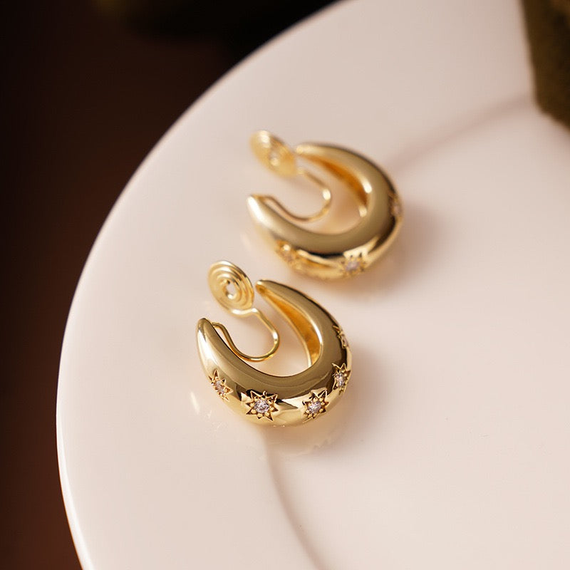 Macro close-up showing the high-shine gold finish and delicate clear cubic zirconia stones set inside deep starburst engravings on a thick hoop clip-on earring.