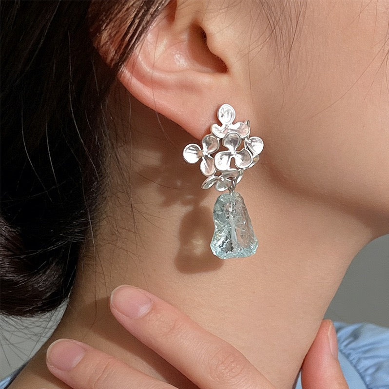 Model wearing matte silver floral earrings with raw icy-blue crystal drops