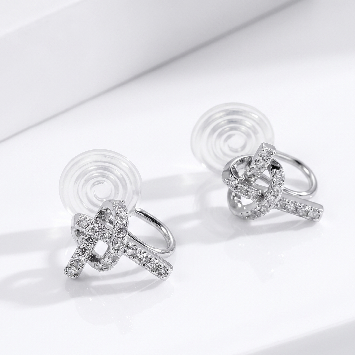 A pair of silver clip-on earrings in a beautifully interwoven knot design, fully encrusted with sparkly pavé diamond-effect stones.
