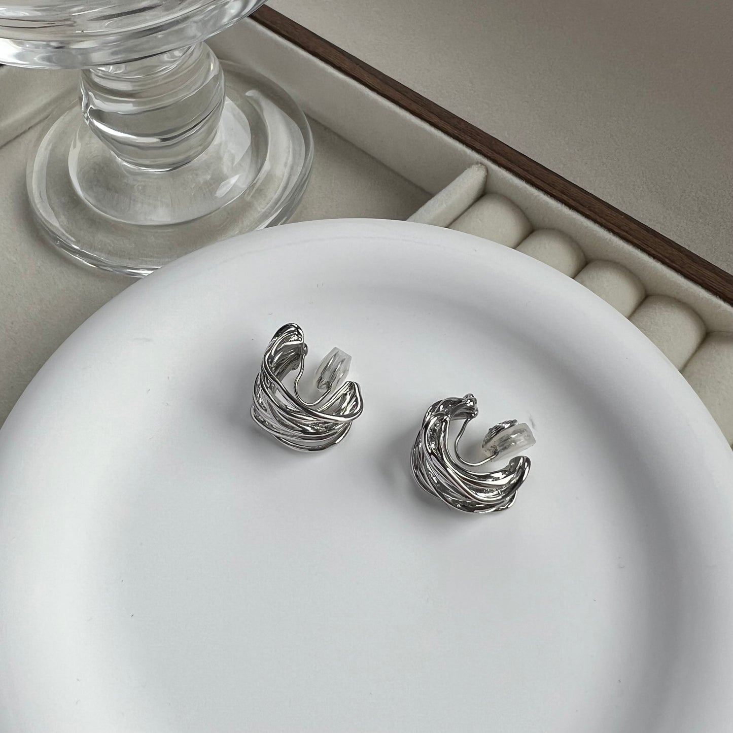 Side profile of a chunky silver clip-on hoop earring, highlighting the thick C-shaped curve and the "huggie" style fit for non-pierced ears.
