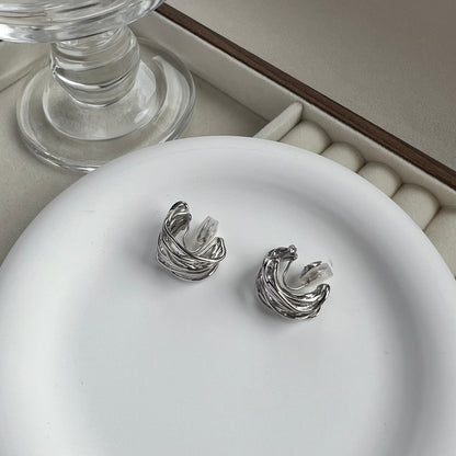 Side profile of a chunky silver clip-on hoop earring, highlighting the thick C-shaped curve and the "huggie" style fit for non-pierced ears.
