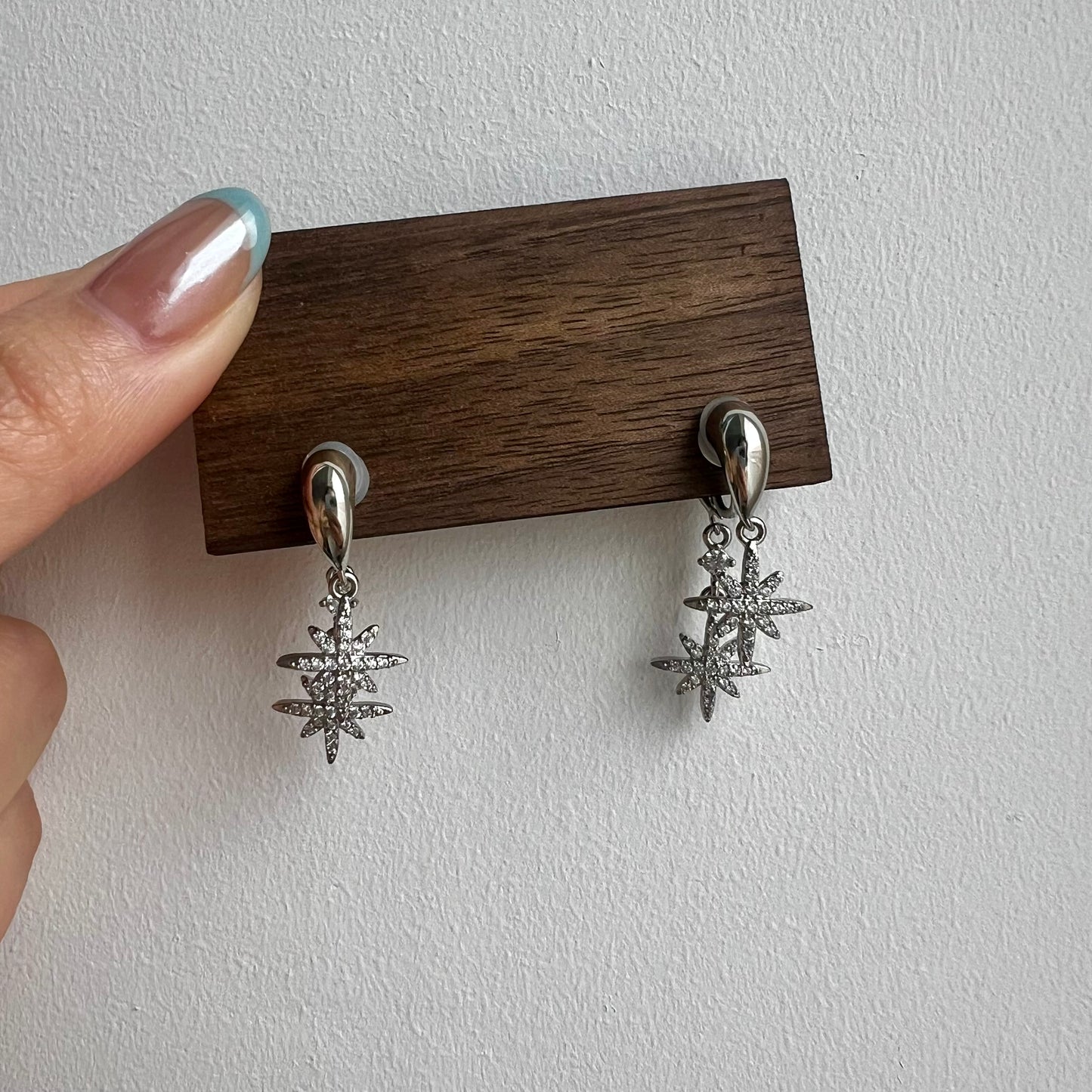 Silver clip-on earring featuring a front diamond-studded star and a second trailing star dropping from behind