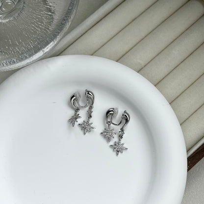 Two silver star front-and-back drop clip-on earrings resting on a branded jewellery display card