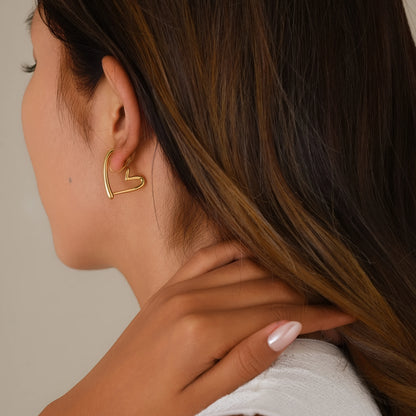 Close-up of model wearing 18k gold chunky heart hoop clip-ons, illustrating the secure and realistic "pierced" fit.