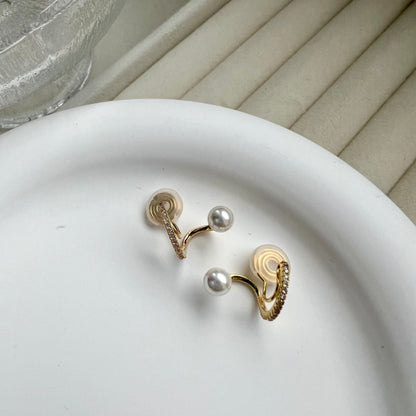 Gold and pearl earrings on a white plate with a neutral background