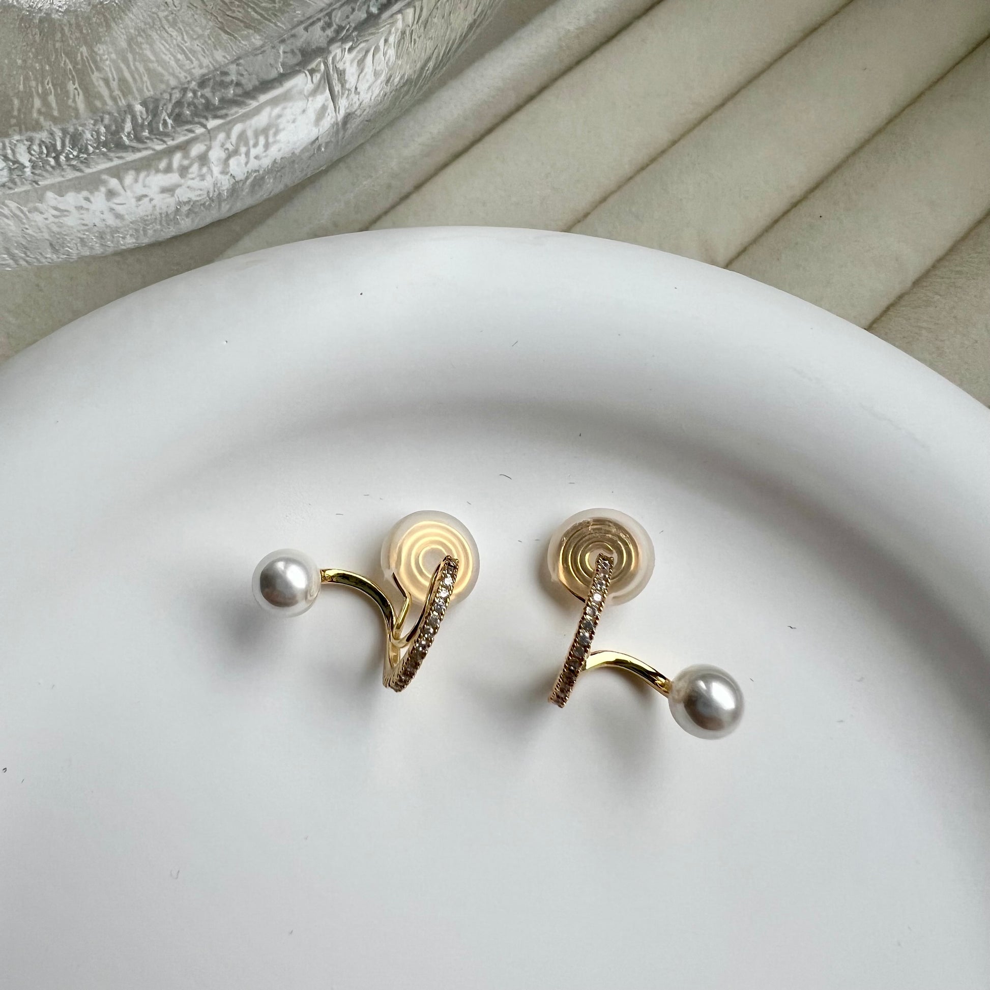 A pair of gold clip-on hoop earrings featuring a suspended white pearl drop against a clean background.