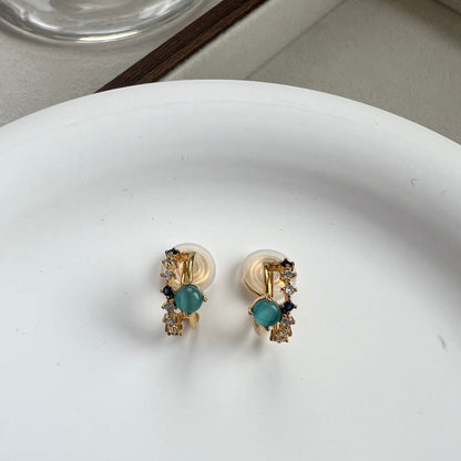 Close-up of dainty 18k gold double hoop clip-on earrings featuring one band of clear pavé diamonds and one band with a single sapphire blue gemstone.