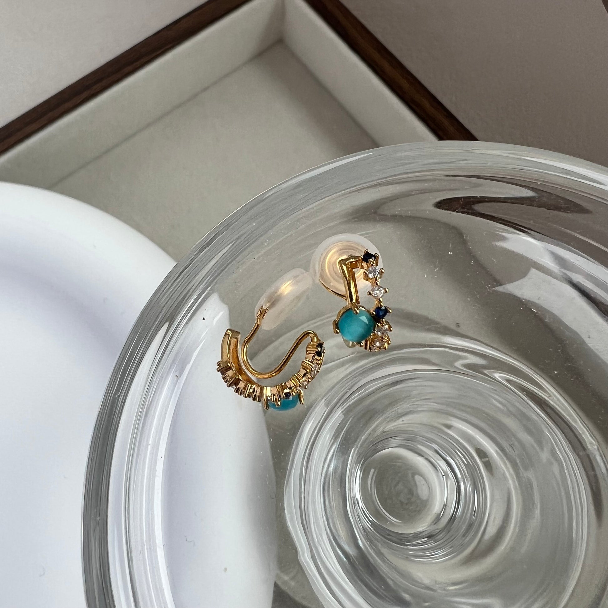 A pair of tiny blue gemstone and diamond double hoop clip-on earrings resting on a neutral linen background