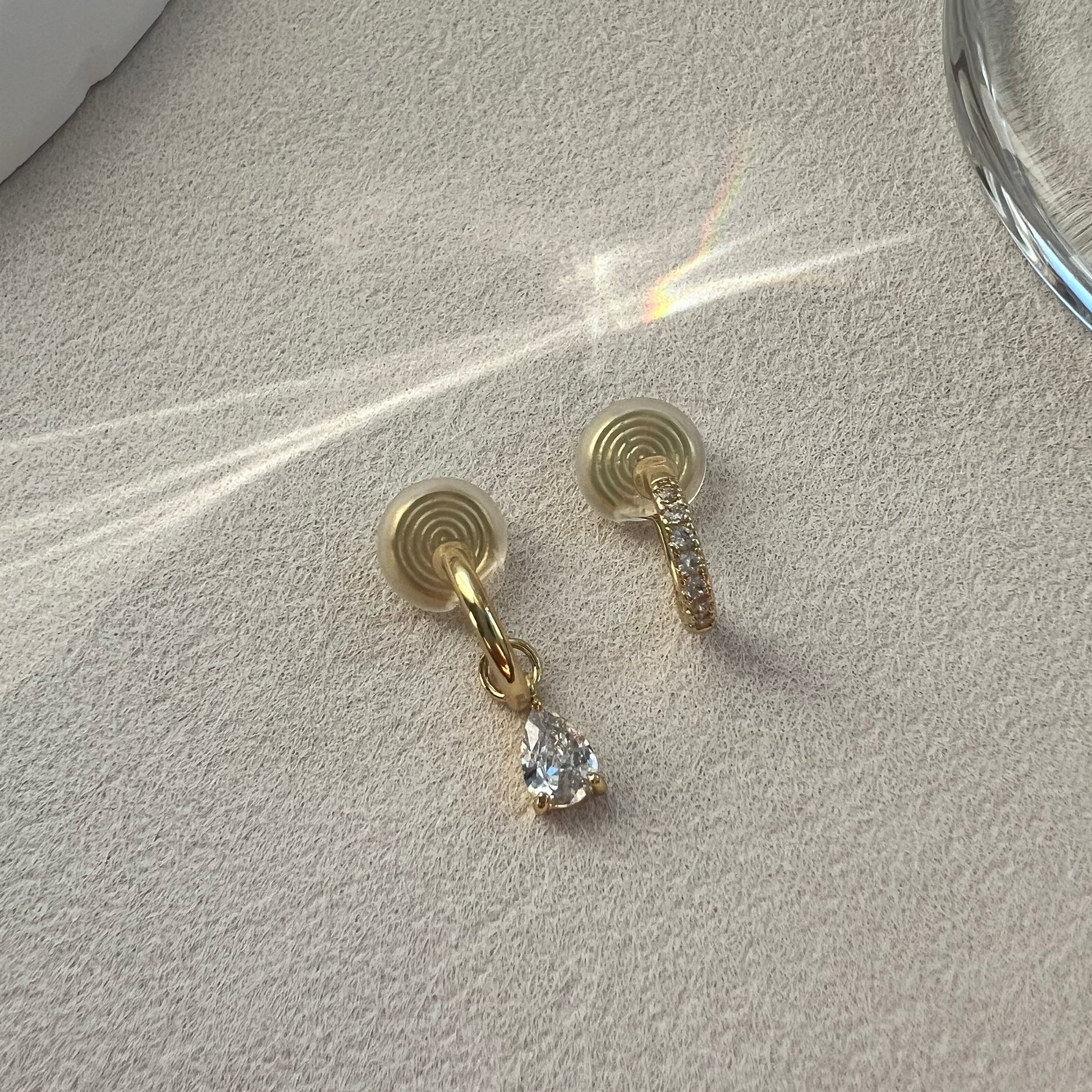 A close-up of a woman's ear wearing a curated stack of diamond clip-on earrings. She is wearing an asymmetrical diamond pave hoop and a diamond drop hoop, styled effortlessly without actual piercings.