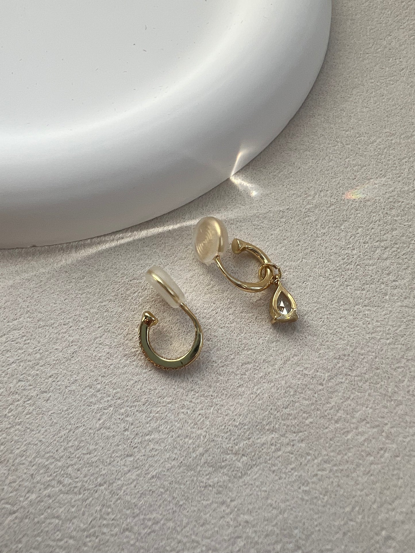 A macro close-up showing the flexible, clear resin U-clip on the back of a sparkling diamond drop earring, designed for a 100% pain-free, comfortable fit.