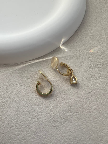 A macro close-up showing the flexible, clear resin U-clip on the back of a sparkling diamond drop earring, designed for a 100% pain-free, comfortable fit.
