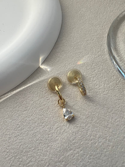 A matching asymmetrical set of two diamond clip-on earrings. One is a classic diamond pave hoop, and the other is a pave hoop with a dangling diamond drop. Both feature clear, invisible resin clips for non-pierced ears