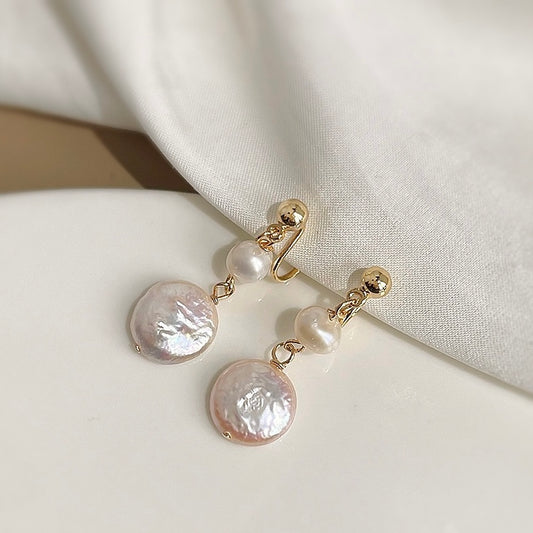 A pair of double drop clip-on earrings featuring a small round freshwater pearl suspended above a larger, textured coin pearl, set with gold-tone hardware against a white background.