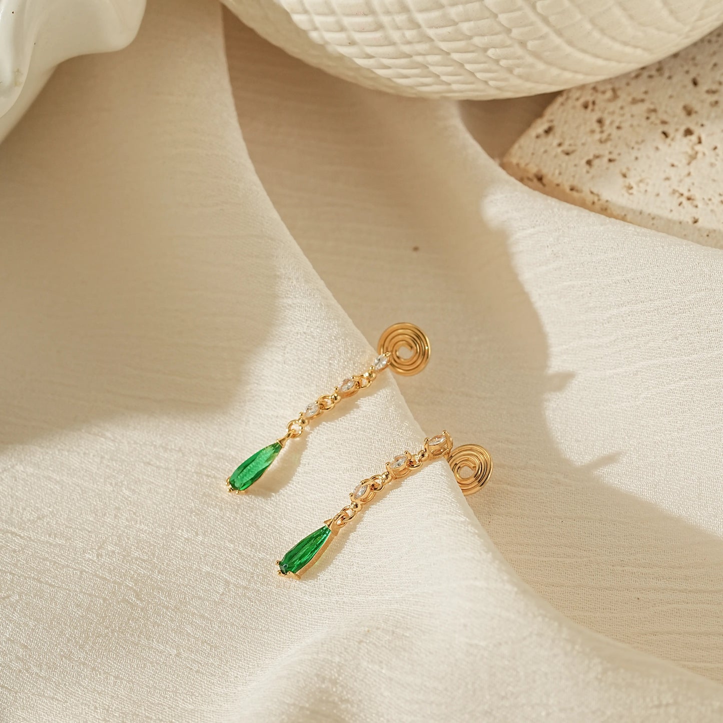 Luxury emerald and gold dangle earrings for non-pierced ears on a creamy background.