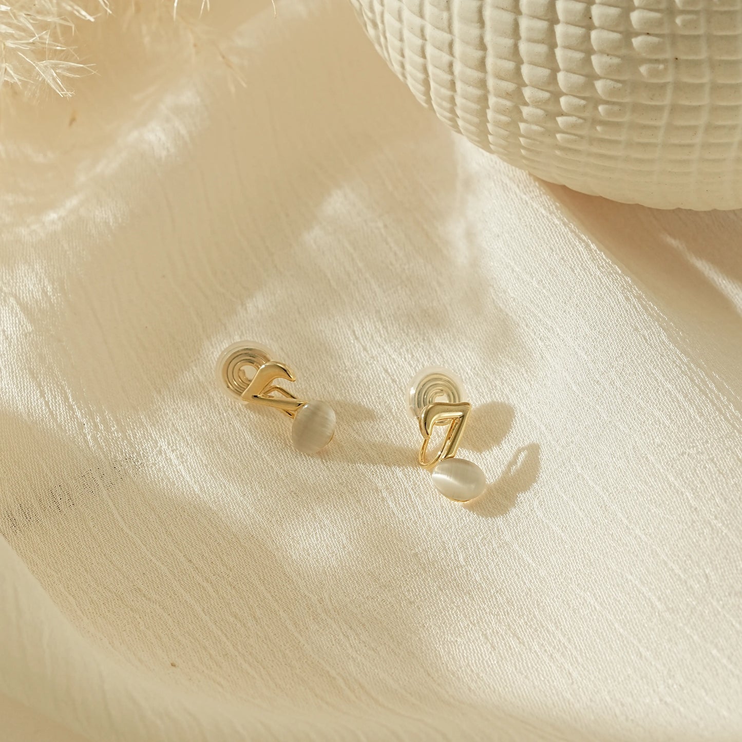 Elegant gold music note earrings for musicians, laid on a creamy background.