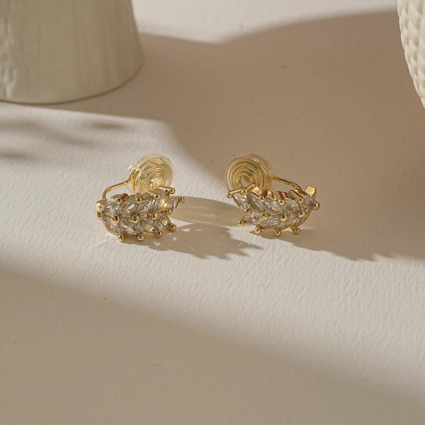Pair of gold wheat diamond earrings on a warm, creamy boutique-style background.