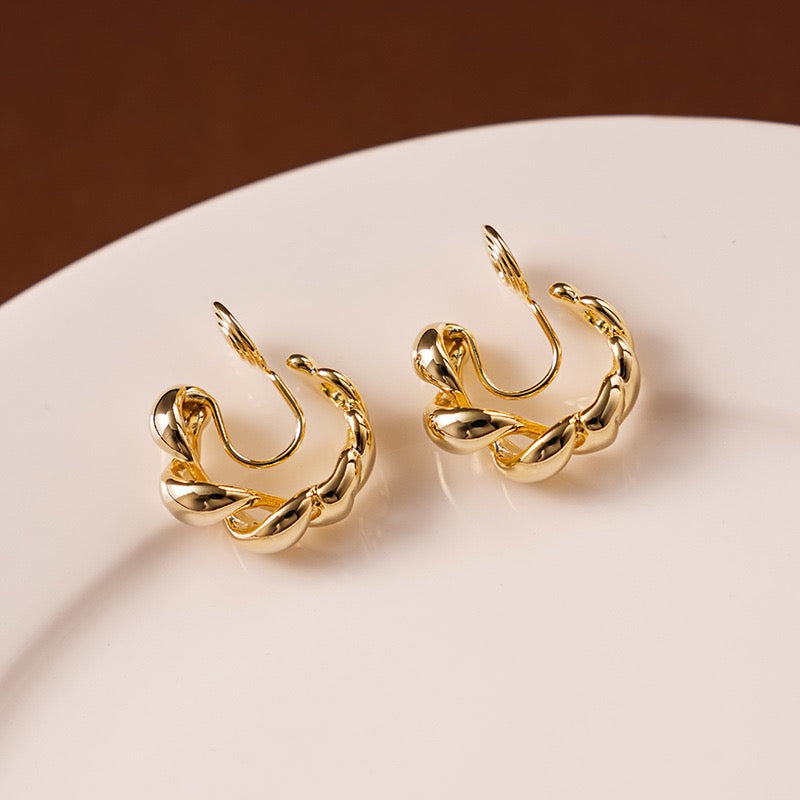 Side profile of a model styling the gold twisted hoop clip-on earrings paired with a minimalist gold ear cuff for a no-piercing ear stack.