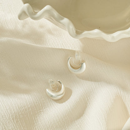Close-up of the non-reflective matte silver texture on minimalist clip-on hoops.