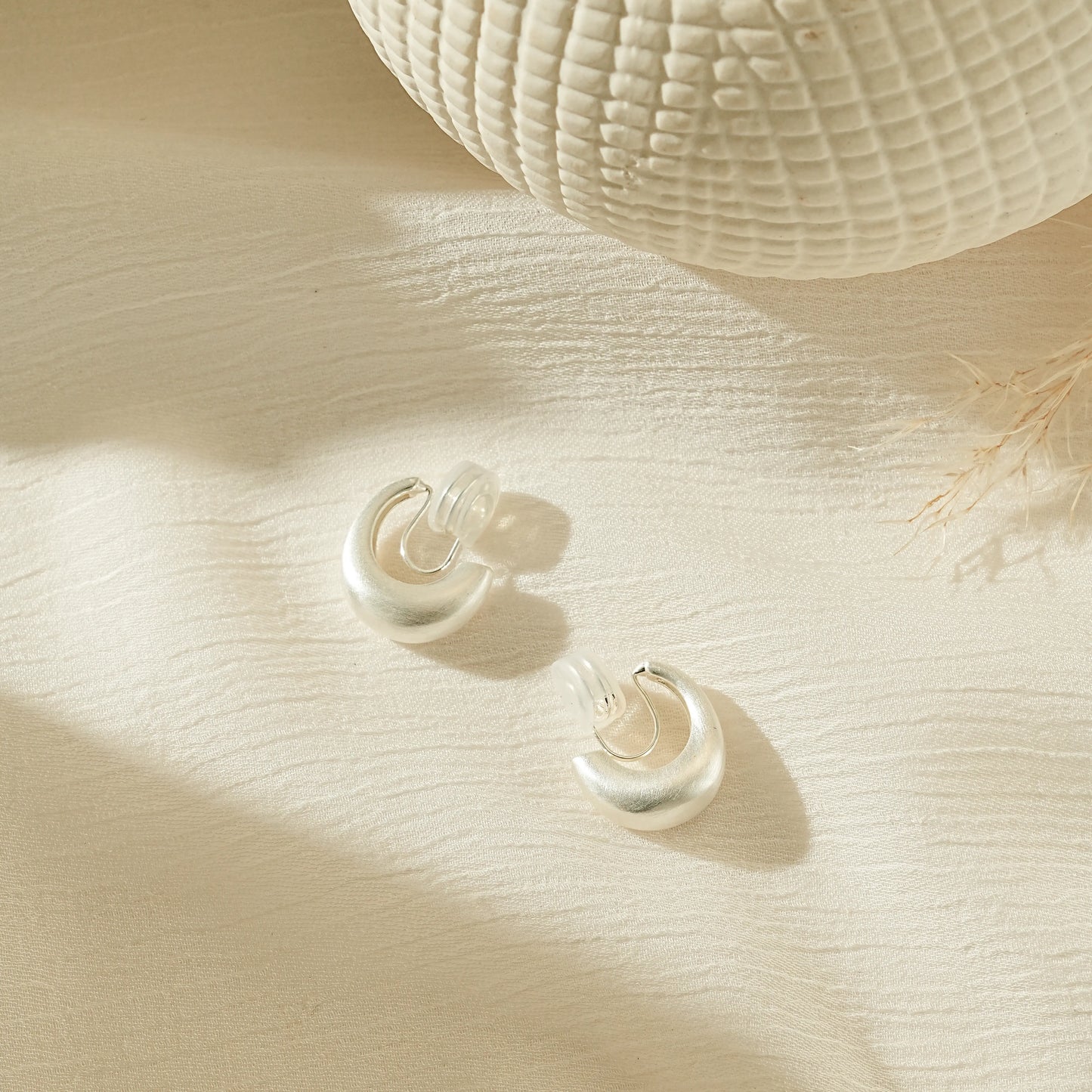 Minimalist matte silver clip-on hoop earrings with a brushed satin finish.