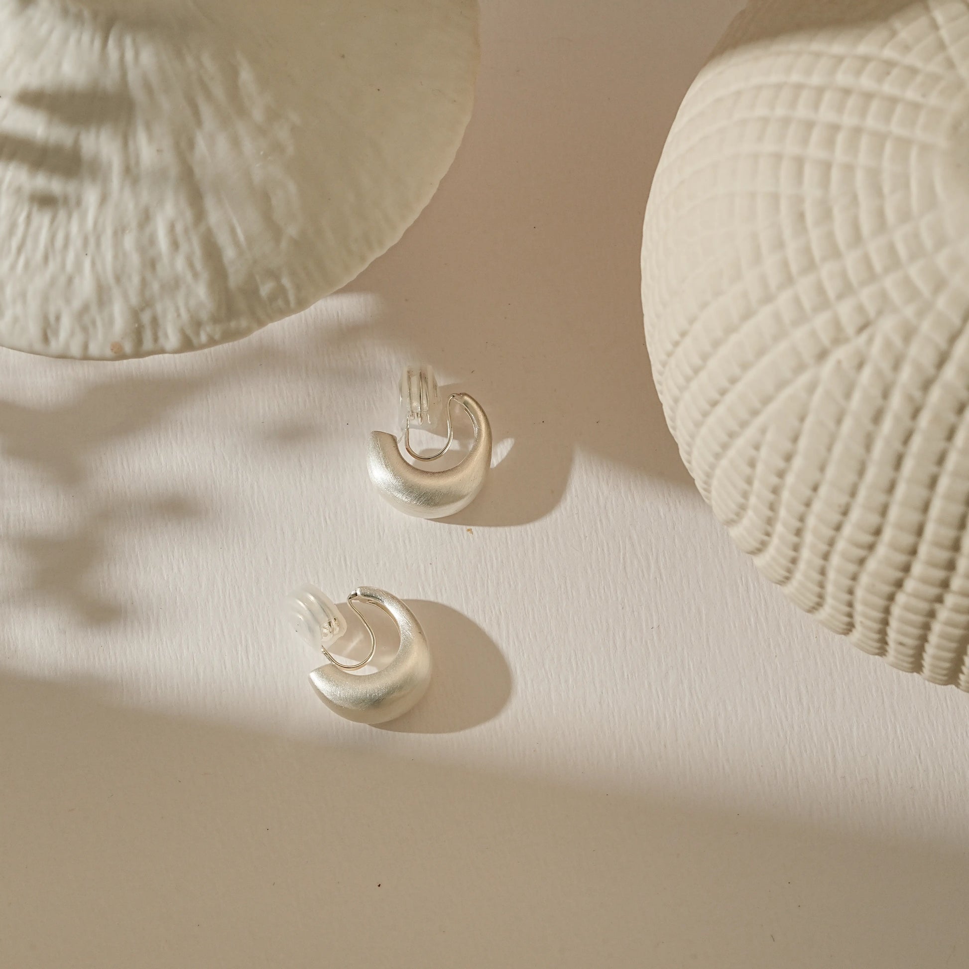 Modern satin silver earrings for non-pierced ears on a clean, creamy background.