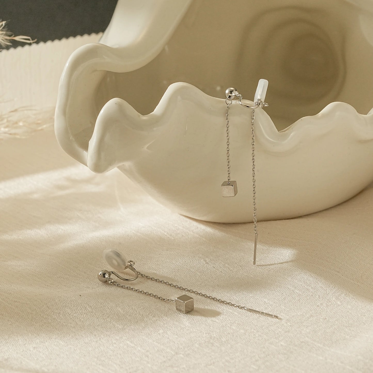 Close-up of silver threader illusion earrings for non-pierced ears, reflecting light.