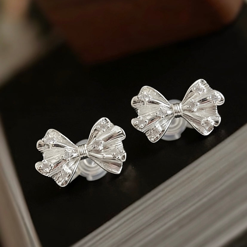 Side profile of a model styling the silver bow clip-on studs as a base piece, paired with a sleek silver ear cuff for a curated, no-piercing ear stack