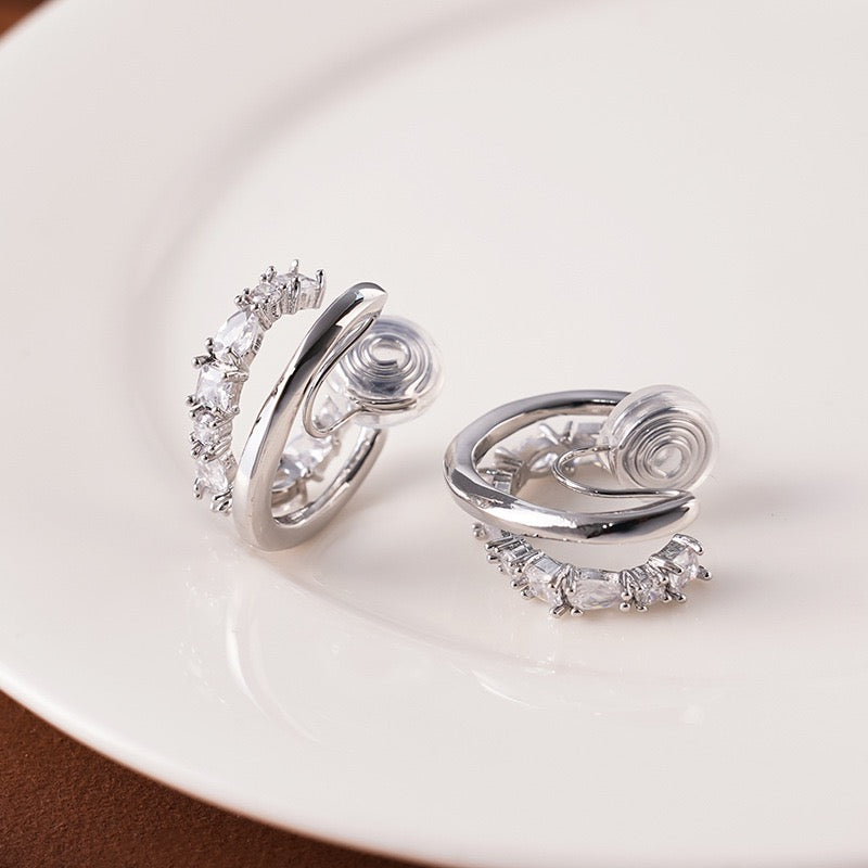 Pair of Earclipse silver double hoop illusion clip-on earrings with one polished band and one crystal-lined band featuring clear silicone cushion pads on a white ceramic dish