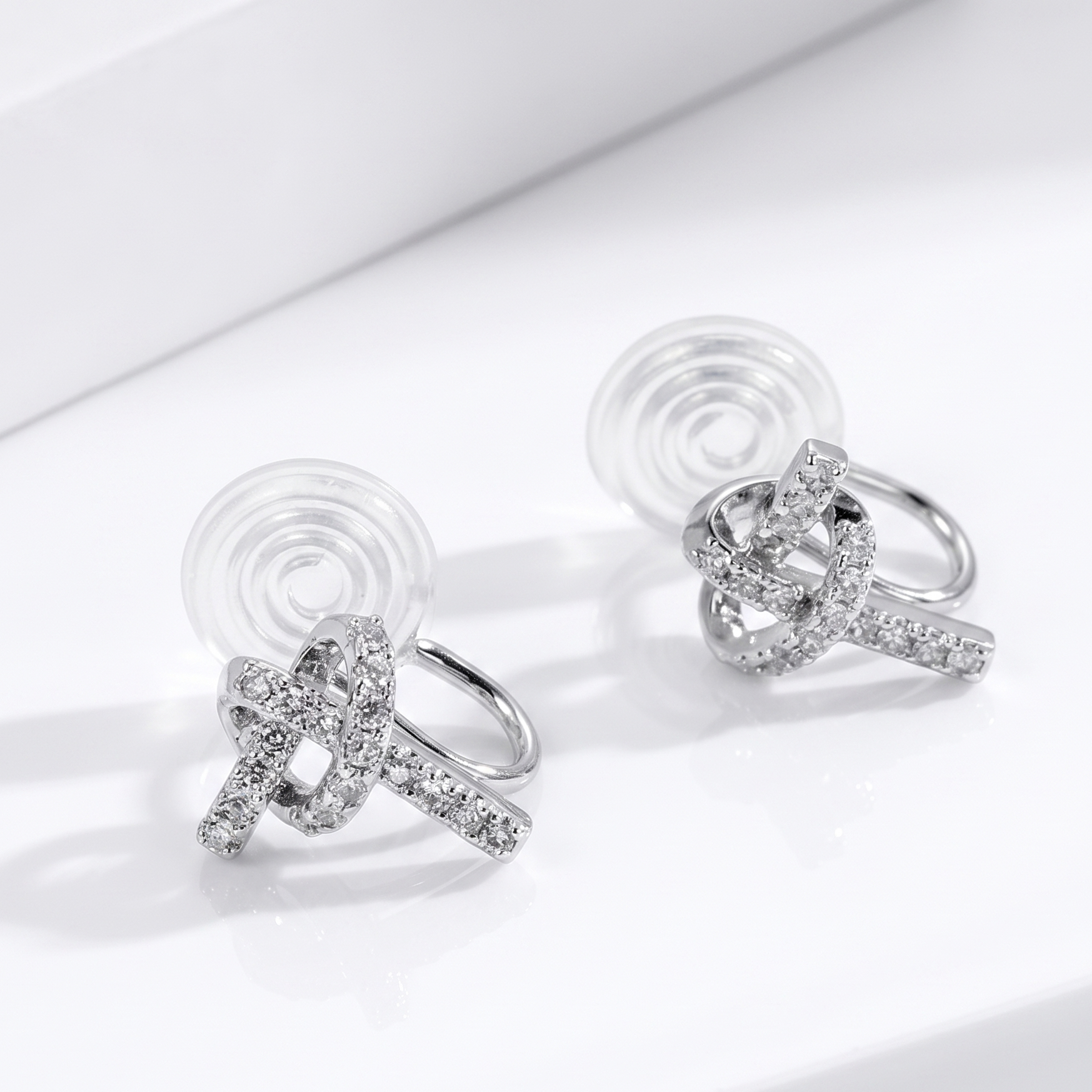 A pair of silver clip-on earrings in a beautifully interwoven knot design, fully encrusted with sparkly pavé diamond-effect stones.