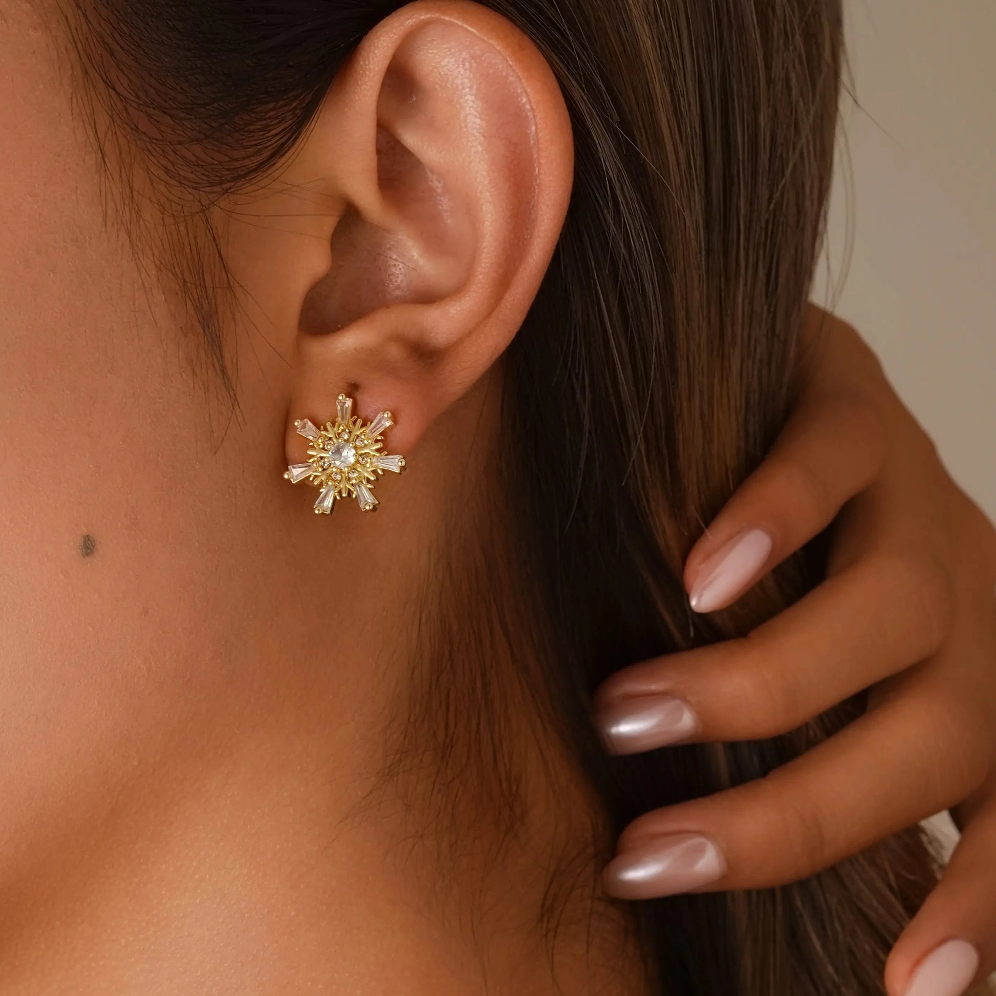 Close-up of model styling the gold snowflake studs, showing the secure and realistic fit.