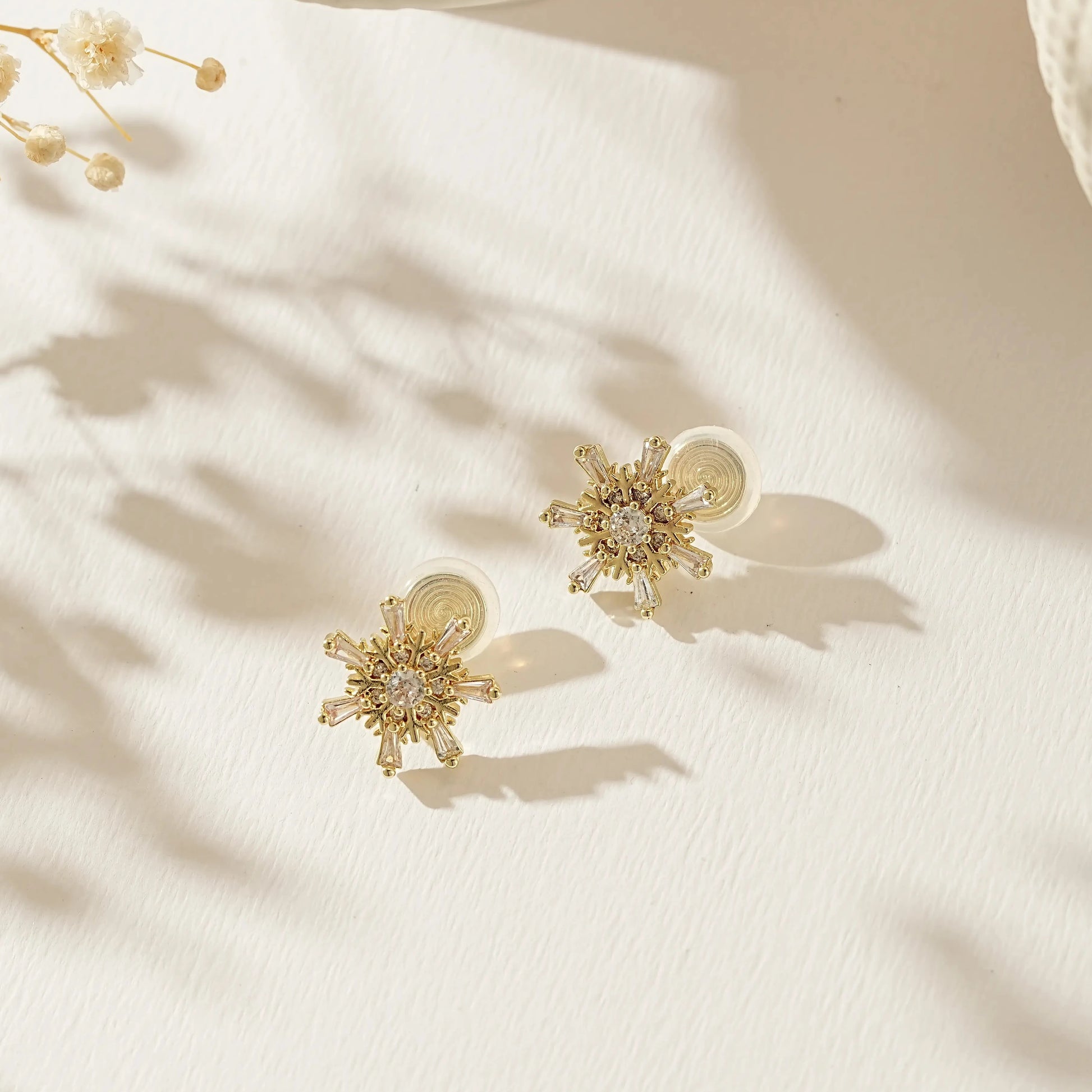 Festive gold snowflake earrings for unpierced ears on a soft, snowy background.
