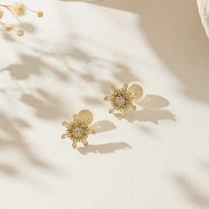 Festive gold snowflake earrings for unpierced ears on a soft, snowy background.