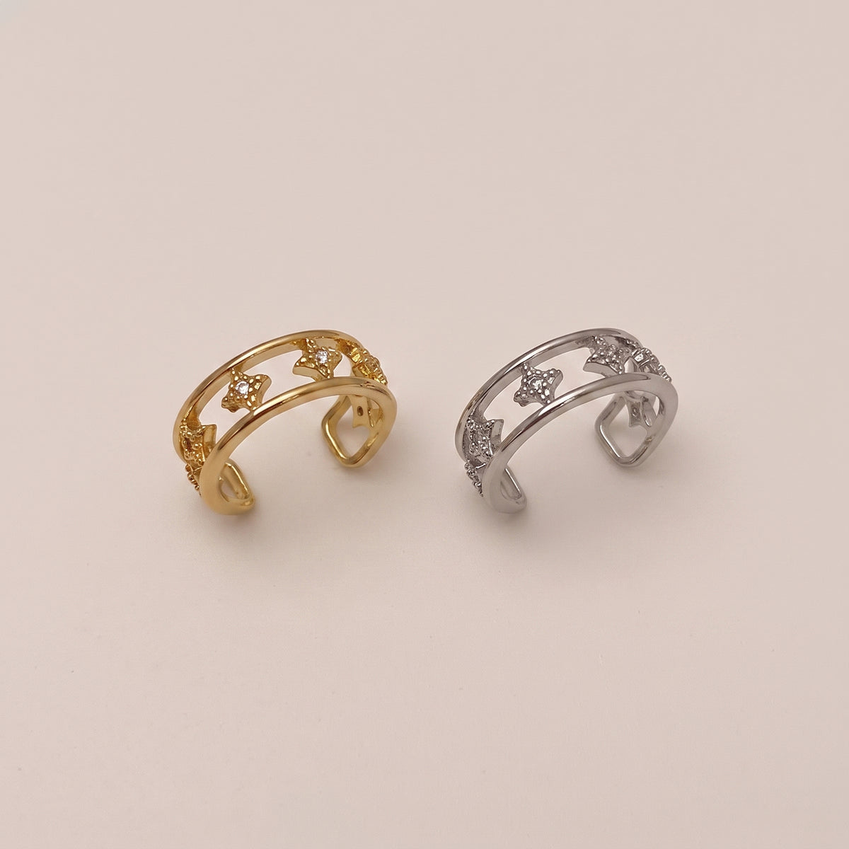 A gold double-band ear cuff featuring small star shapes set with clear cubic zirconia crystals, resting against a neutral background.
