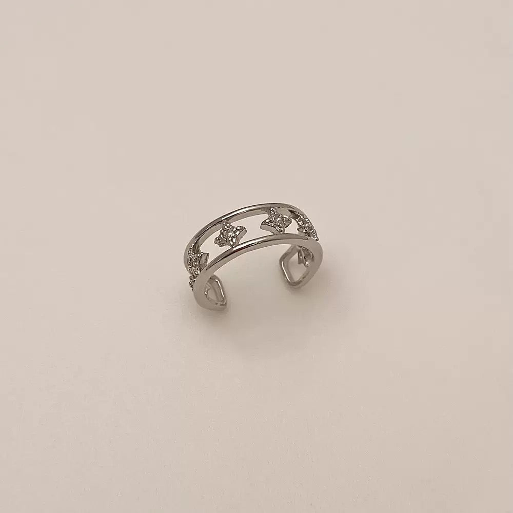 A silver double-band ear cuff featuring small star shapes set with clear cubic zirconia crystals, resting against a neutral background.