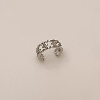 A silver double-band ear cuff featuring small star shapes set with clear cubic zirconia crystals, resting against a neutral background.