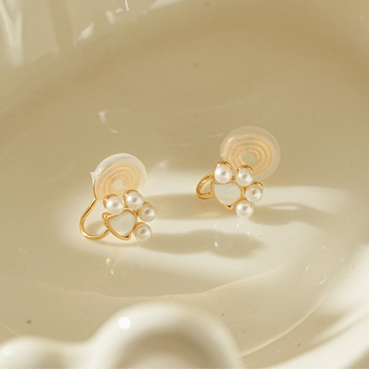 Close-up of gold paw print earrings with a pearl center for unpierced ears.