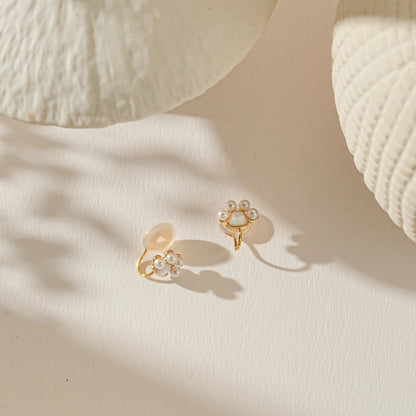 Gold and pearl paw print clip-on earrings on a warm creamy background.