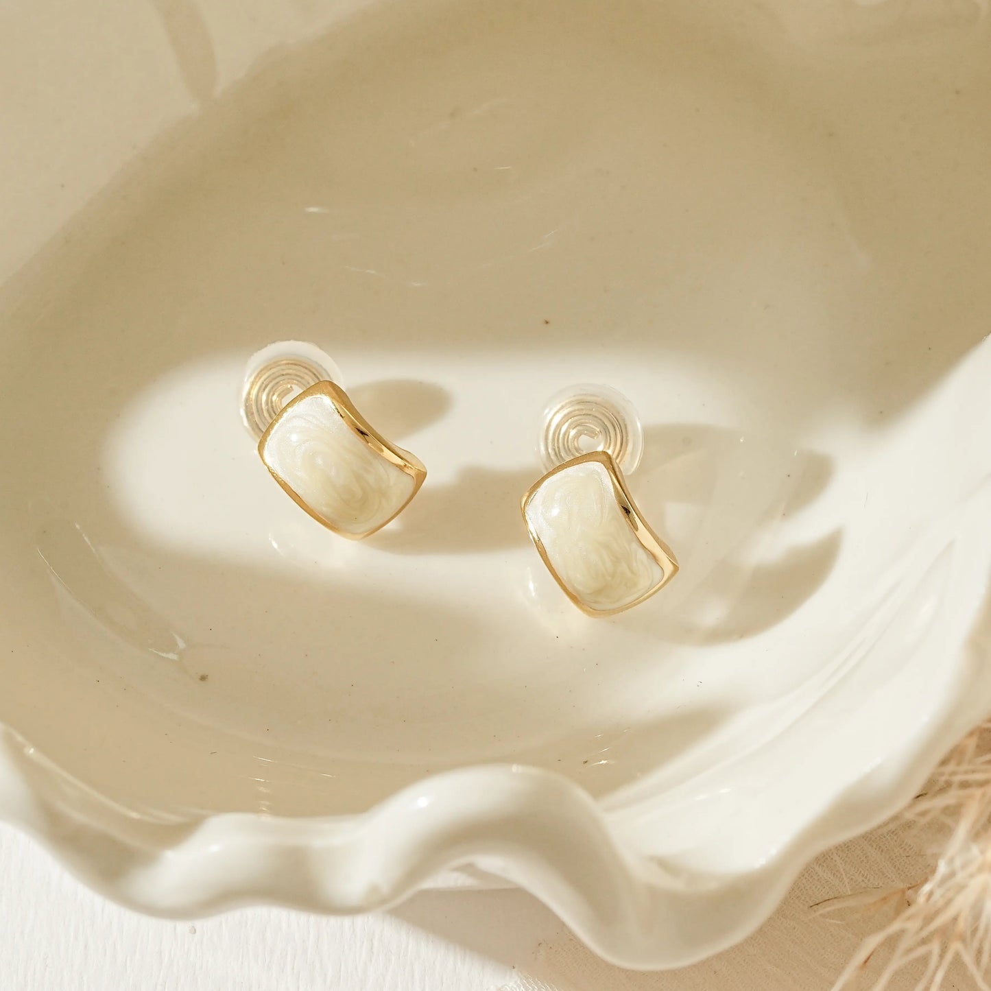 Close-up of the smooth, hand-painted white enamel detail on gold clip-on studs.