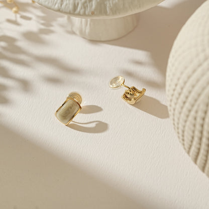 Modern minimalist white enamel and gold clip-on earrings on a creamy background.