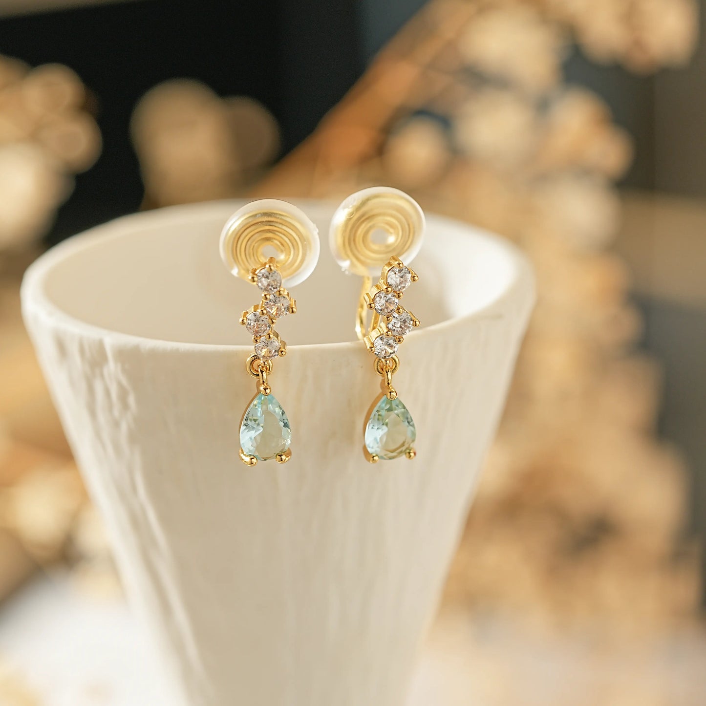 Aquamarine teardrop gemstone close-up showing the faceted blue stone in a polished gold finish clip-on setting.