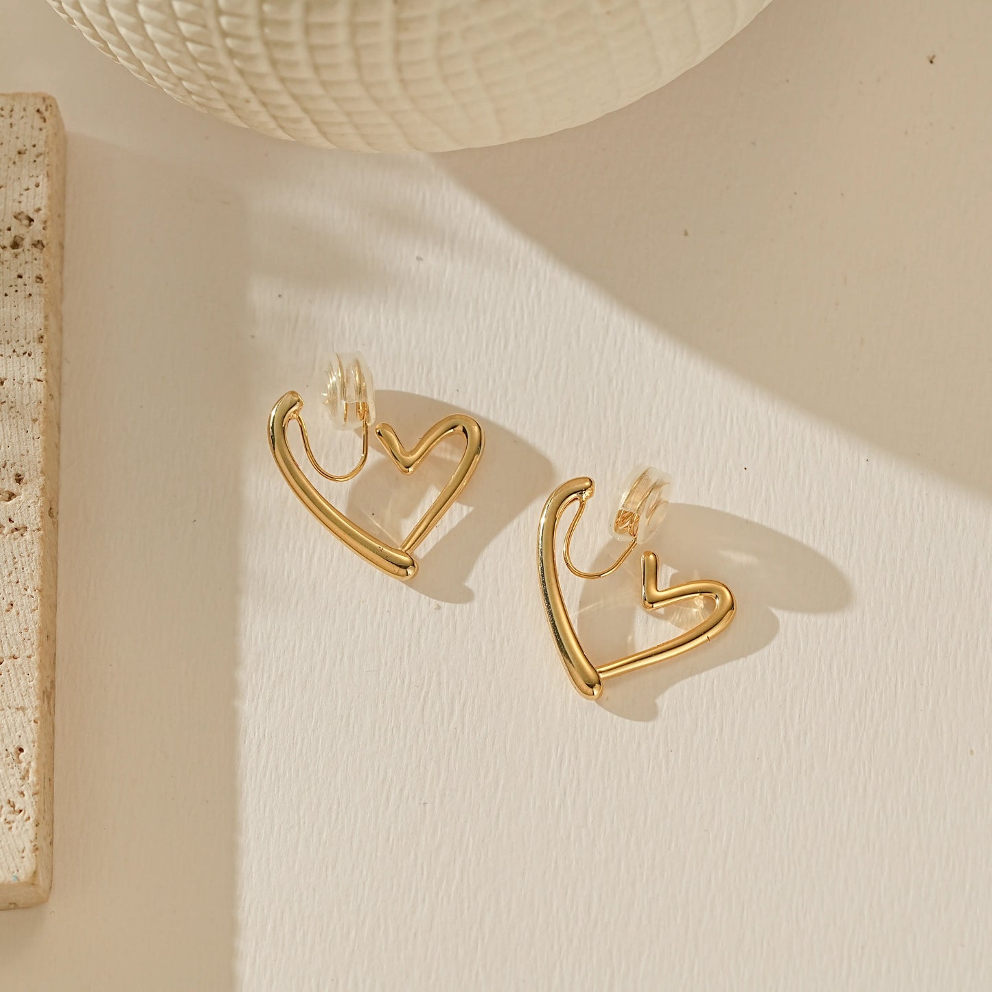 Angled view of polished 18k gold Love Heart clip-on hoop, reflecting warm light on the curved surface.