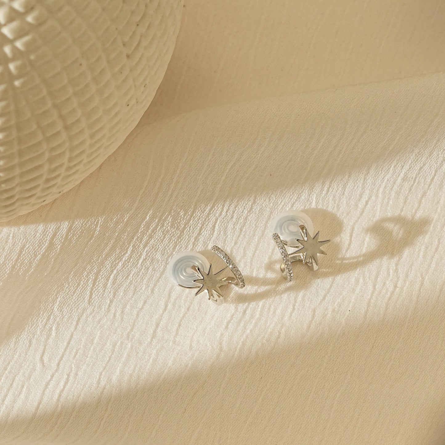 Pair of silver star clip-on hoops laid flat, showing the star and diamond detail.