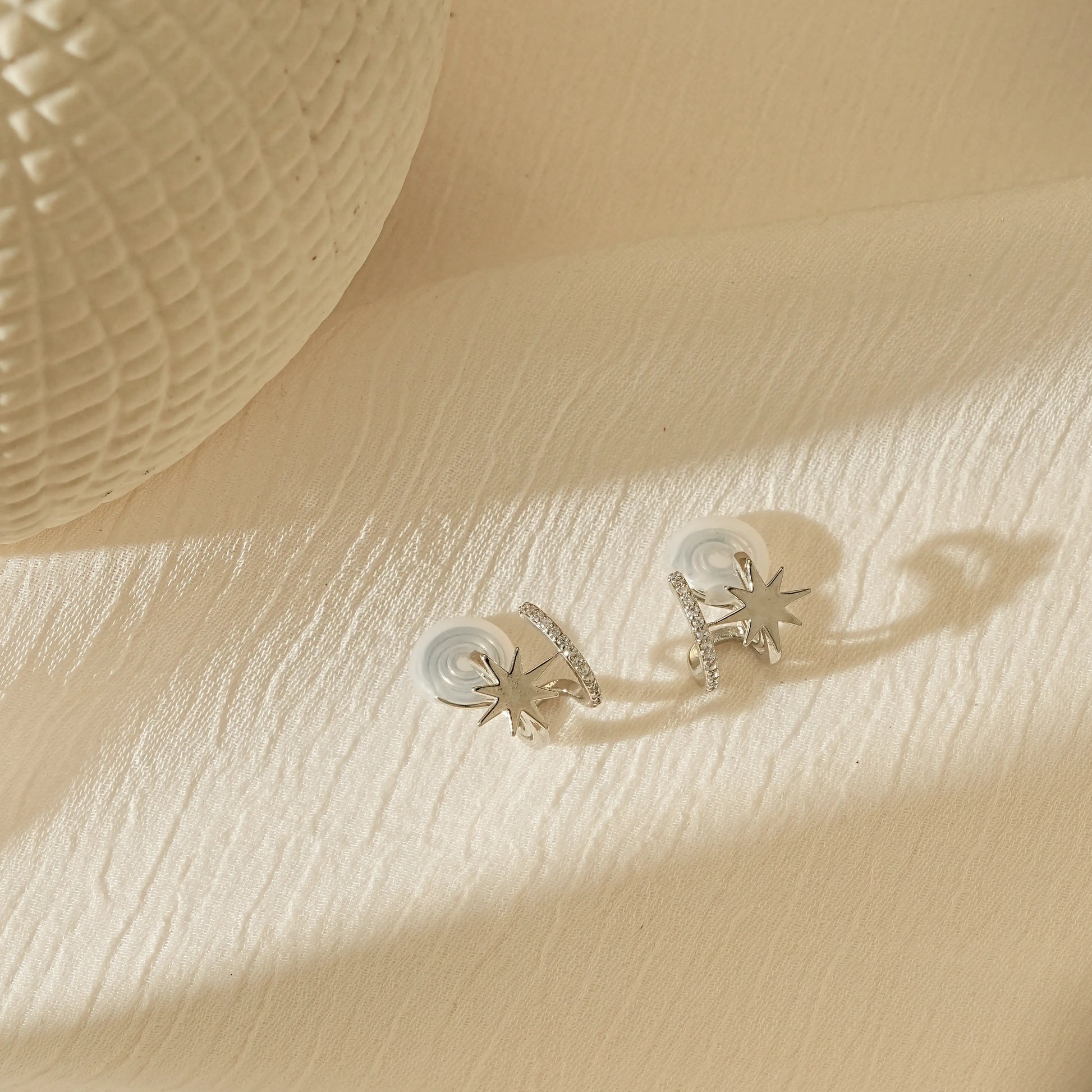 Pair of silver star clip-on hoops laid flat, showing the star and diamond detail.