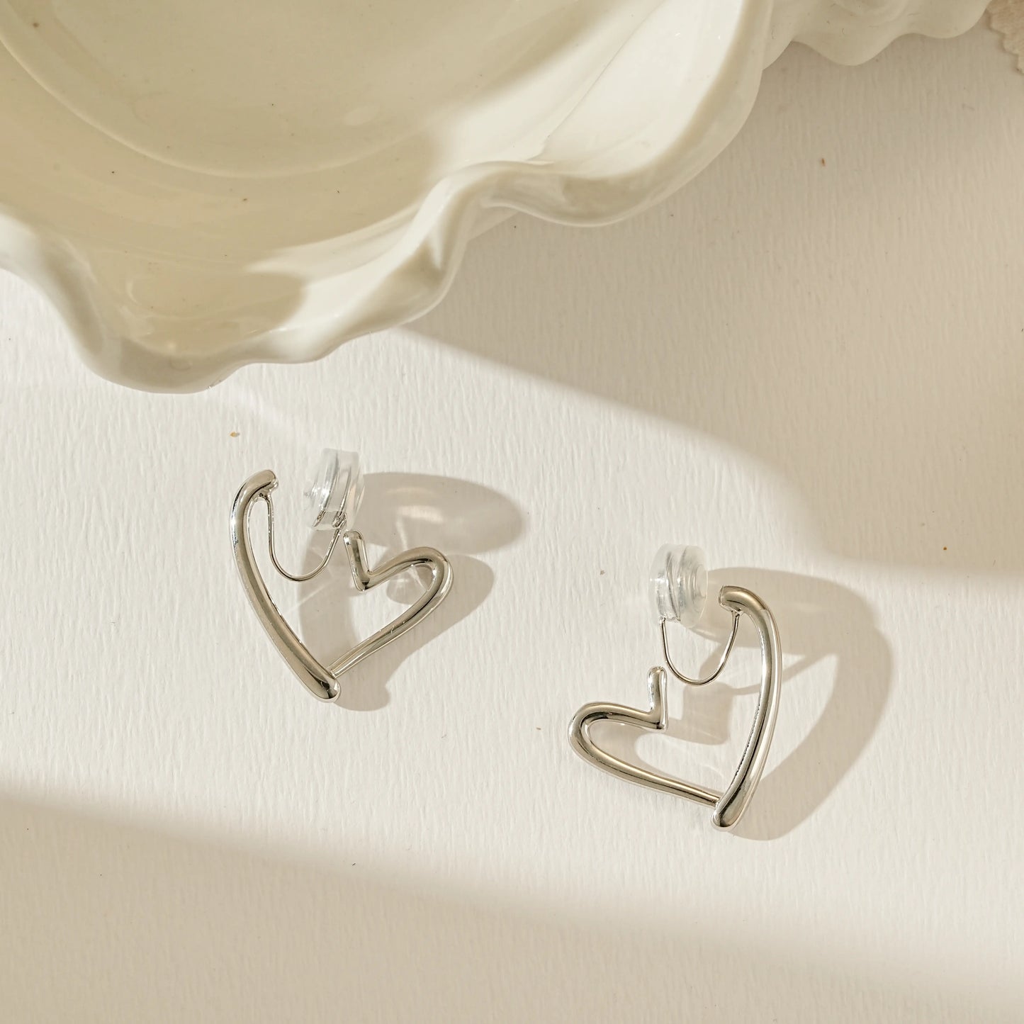 Angled view of polished silver Love Heart clip-on hoop, reflecting light on the curved surface.