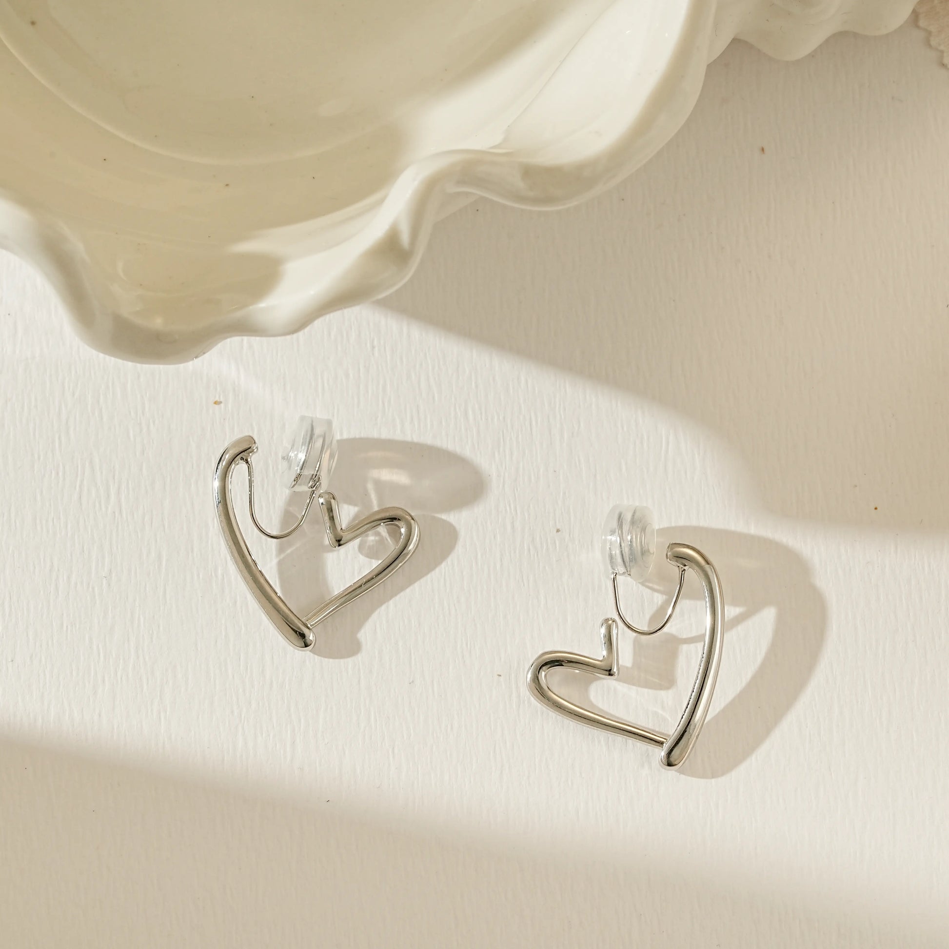 Angled view of polished silver Love Heart clip-on hoop, reflecting light on the curved surface.